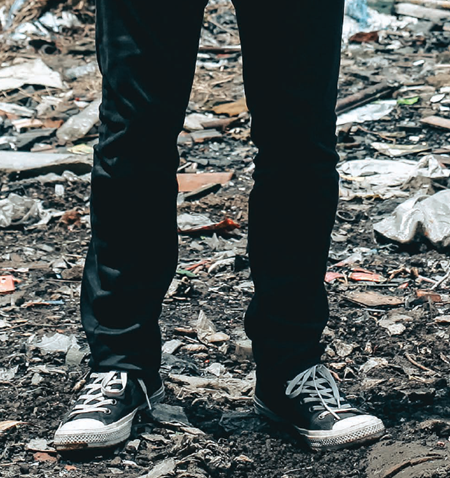 A pair of legs in jeans and shoes standing on a pile of leaves.