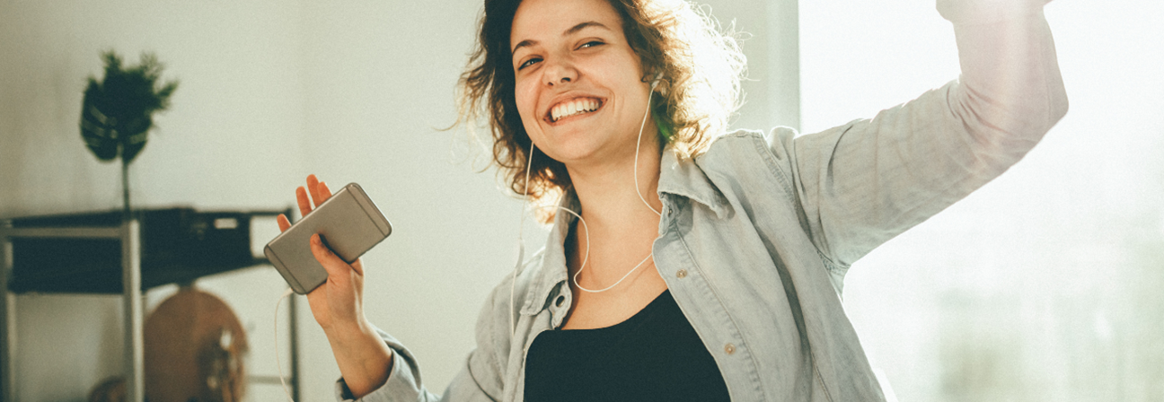 A woman with headphones on holding a phone.