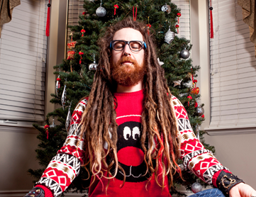 A person wearing a red and white sweater and glasses standing in front of a christmas tree.