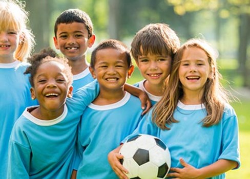 A group of smiling kids in blue shirts with a soccer ball.